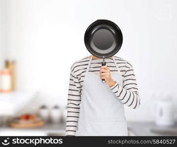 people, cooking, culinary and identity concept - man or cook in apron hiding his face behind frying pan over home kitchen background