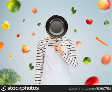 people, cooking, culinary and identity concept - man or cook in apron hiding his face behind frying pan over gray background with falling vegetables