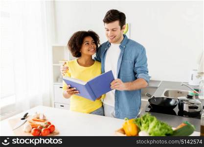 people, cooking food and healthy eating concept - happy couple with cookbook and vegetables at home kitchen. happy couple with cooking book at home kitchen