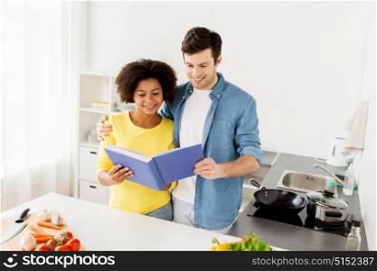 people, cooking food and healthy eating concept - happy couple with cookbook and vegetables at home kitchen. happy couple with cooking book at home kitchen