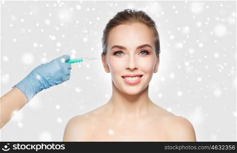 people, cosmetology, plastic surgery and beauty concept - beautiful young woman face and beautician hand in glove with syringe making injection over gray background and snow