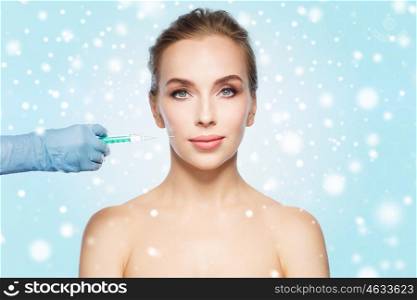 people, cosmetology, plastic surgery and beauty concept - beautiful young woman face and beautician hand in glove with syringe making injection over blue background and snow