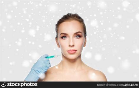 people, cosmetology, plastic surgery and beauty concept - beautiful young woman face and beautician hand in glove with syringe making injection over gray background and snow