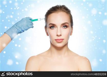 people, cosmetology, plastic surgery and beauty concept - beautiful young woman face and beautician hand in glove with syringe making injection over blue background and snow