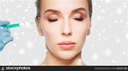 people, cosmetology, plastic surgery and beauty concept - close up of beautiful young woman face and beautician hand in glove with syringe making injection over gray background and snow