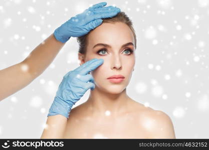 people, cosmetology, plastic surgery and beauty concept - surgeon or beautician hands touching woman face over gray background and snow