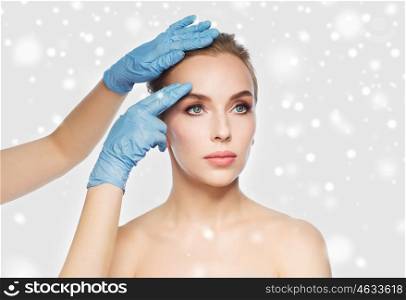 people, cosmetology, plastic surgery and beauty concept - surgeon or beautician hands touching woman face over gray background and snow