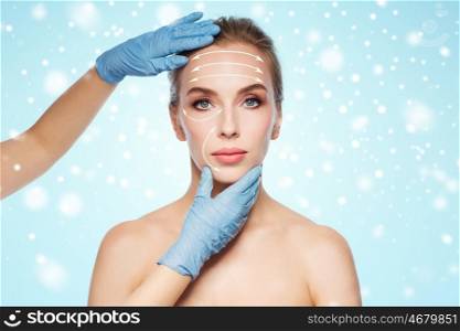 people, cosmetology, plastic surgery and beauty concept - surgeon or beautician hands touching woman face with lifting arrows over blue background and snow