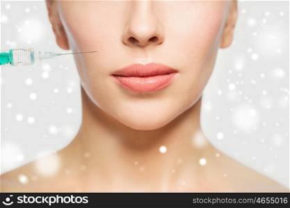 people, cosmetology, plastic surgery, anti-aging and beauty concept - close up of beautiful young woman face and syringe making injection over gray background and snow