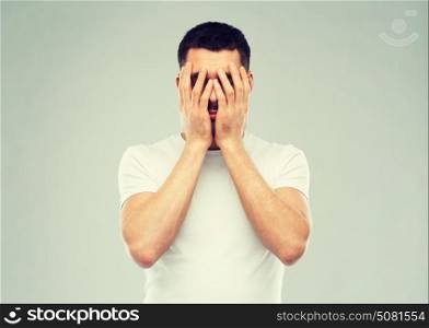 people, crisis, emotions and stress concept - man in white t-shirt covering his face with hands over gray background. man in white t-shirt covering his face with hands