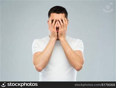 people, crisis, emotions and stress concept - man in white t-shirt covering his face with hands over gray background