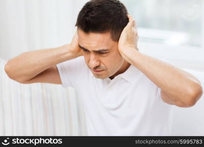 people, crisis, emotions, noise and stress concept - unhappy man closing his ears by hands at home