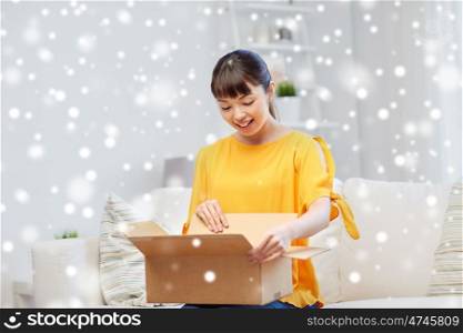 people, delivery, commerce, shipping and shopping concept - happy asian young woman with cardboard parcel box at home over snow