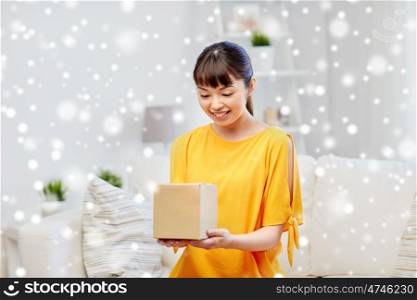 people, delivery, commerce, shipping and shopping concept - happy asian young woman with cardboard parcel box at home over snow
