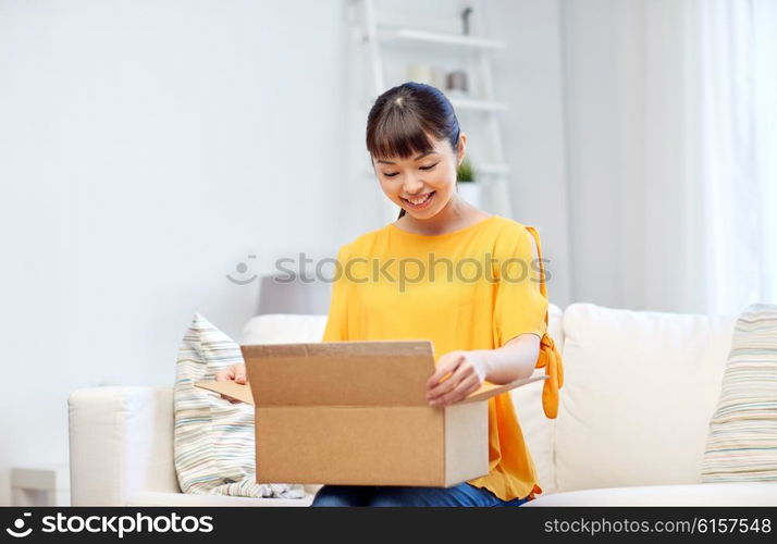 people, delivery, commerce, shipping and shopping concept - happy asian young woman with cardboard parcel box at home