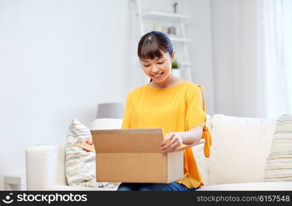 people, delivery, commerce, shipping and shopping concept - happy asian young woman with cardboard parcel box at home