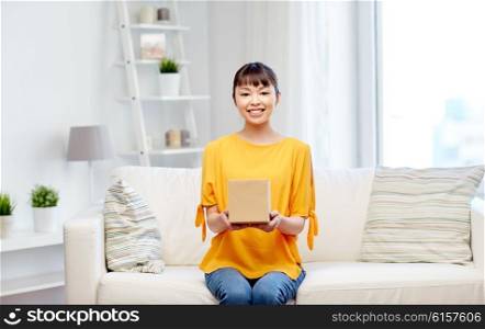 people, delivery, commerce, shipping and shopping concept - happy asian young woman with cardboard parcel box at home