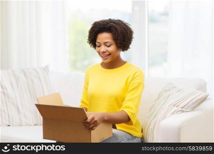 people, delivery, shipping and postal service concept - happy african american young woman opening cardboard box or parcel at home