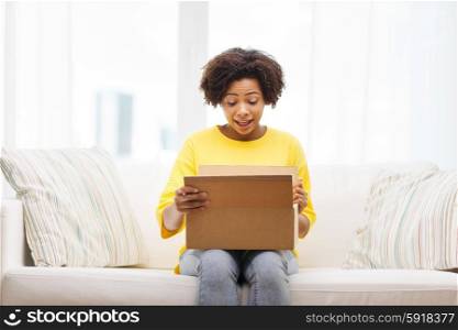 people, delivery, shipping and postal service concept - happy african american young woman opening cardboard box or parcel at home