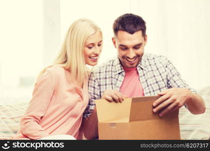 people, delivery, shipping and postal service concept - happy couple opening cardboard box or parcel at home