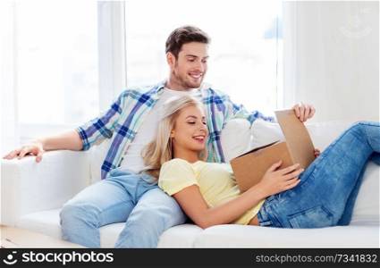people, delivery, shipping and postal service concept - happy couple opening cardboard box or parcel at home. happy couple opening parcel box at home