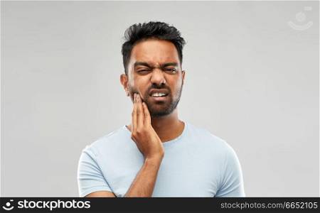 people, dentistry and health problem concept - indian man suffering from toothache over grey background. indian man suffering from toothache