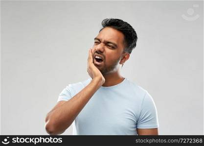 people, dentistry and health problem concept - indian man suffering from toothache over grey background. indian man suffering from toothache