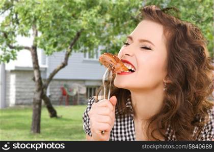 people, diet and food concept - hungry young woman eating meat on fork over house and summer garden background