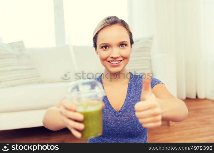 people, diet and healthy lifestyle concept - happy woman with cup of smoothie at home and showing thumbs up. happy woman with cup of smoothie showing thumbs up
