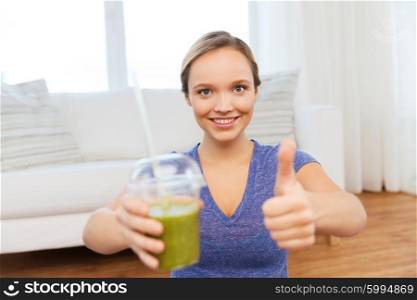 people, diet and healthy lifestyle concept - happy woman with cup of smoothie at home and showing thumbs up