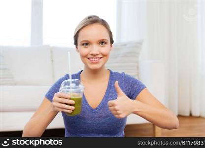 people, diet and healthy lifestyle concept - happy woman with cup of smoothie at home and showing thumbs up