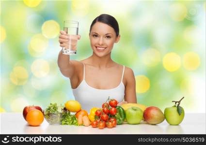 people, diet, healthy eating and food concept - happy woman with glass of water, fruits and vegetables on table over green summer lights background. happy woman with glass of water and healthy food