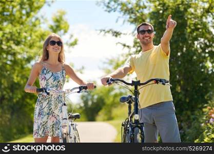 people, direction and lifestyle concept - happy young couple with bicycles at country in summer. happy young couple with bicycles outdoors