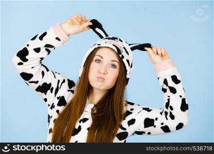 People dressed up like animals concept. Happy teenage girl in funny nightclothes cow pajamas costume, pyjamas cartoon style, smiling positive face expression, studio shot on blue.. Happy crazy woman in cow costume