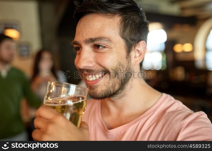 people, drinks, alcohol and leisure concept - close up of happy young man drinking beer at bar or pub