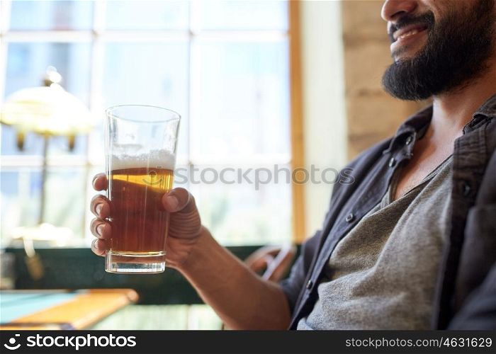 people, drinks, alcohol and leisure concept - close up of happy young man drinking beer from glass at bar or pub