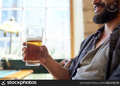 people, drinks, alcohol and leisure concept - close up of happy young man drinking beer from glass at bar or pub
