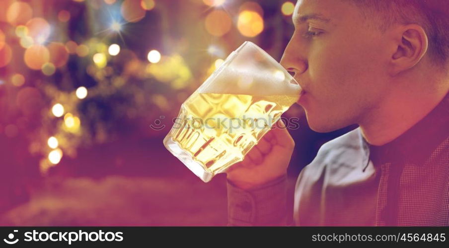people, drinks, alcohol and leisure concept - close up of young man drinking beer from glass mug over holidays lights background