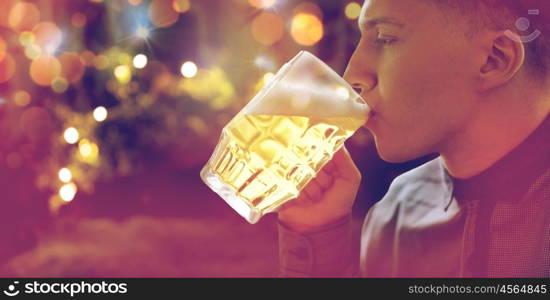 people, drinks, alcohol and leisure concept - close up of young man drinking beer from glass mug over holidays lights background