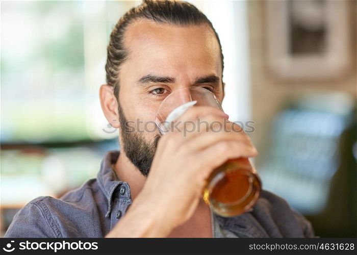 people, drinks, alcohol and leisure concept - close up of young man drinking beer from glass at bar or pub