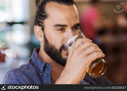 people, drinks, alcohol and leisure concept - happy young man drinking beer from glass at bar or pub