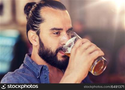 people, drinks, alcohol and leisure concept - happy young man drinking beer from glass at bar or pub. happy man drinking beer at bar or pub. happy man drinking beer at bar or pub