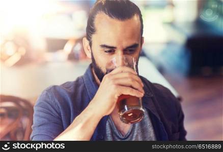 people, drinks, alcohol and leisure concept - happy young man drinking beer from glass at bar or pub. happy man drinking beer at bar or pub. happy man drinking beer at bar or pub