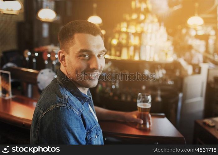 people, drinks, alcohol and leisure concept - happy young man drinking beer at bar or pub