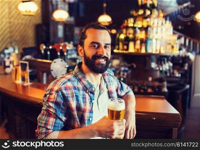 people, drinks, alcohol and leisure concept - happy young man drinking beer at bar or pub