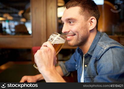 people, drinks, alcohol and leisure concept - happy young man drinking draft beer at bar or pub