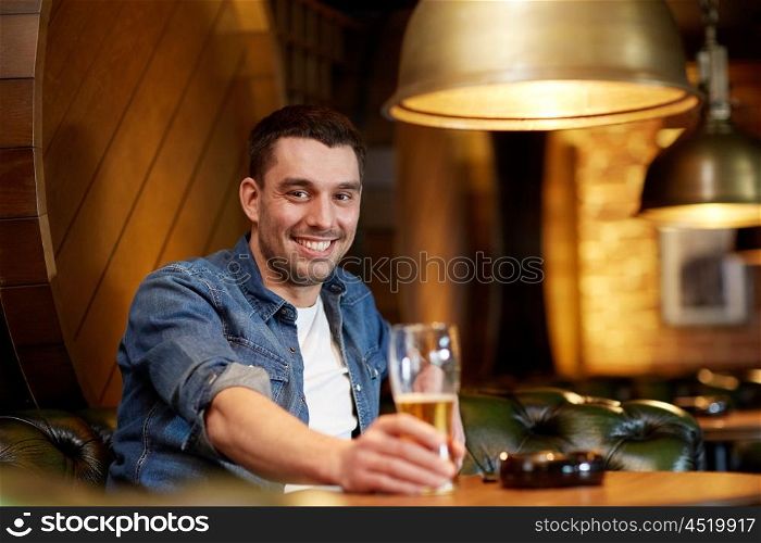people, drinks, alcohol and leisure concept - happy young man drinking draft beer at bar or pub