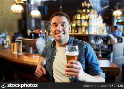 people, drinks, alcohol and leisure concept - happy young man drinking draft beer at bar or pub counter