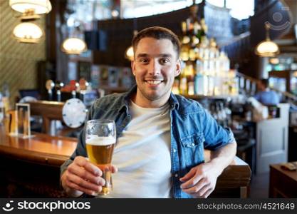 people, drinks, alcohol and leisure concept - happy young man drinking draft beer at bar or pub counter