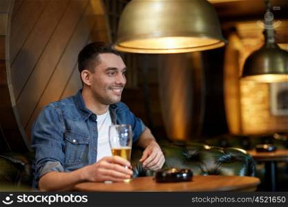 people, drinks, alcohol and leisure concept - happy young man drinking draft beer at bar or pub